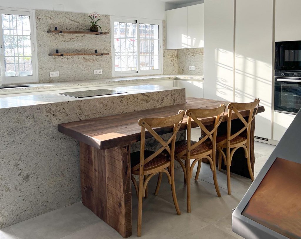 Cocina moderna con isla y encimera de piedra natural y mesa y sillas de madera rústica